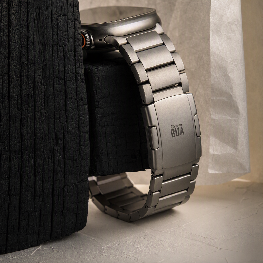 AI-generated Bavarian BUA product shot: a brushed titanium Apple Watch Ultra bracelet propped against charred shou-sugi-ban wood on a pale concrete surface, with the Bavarian BUA mark laser-etched on the clasp