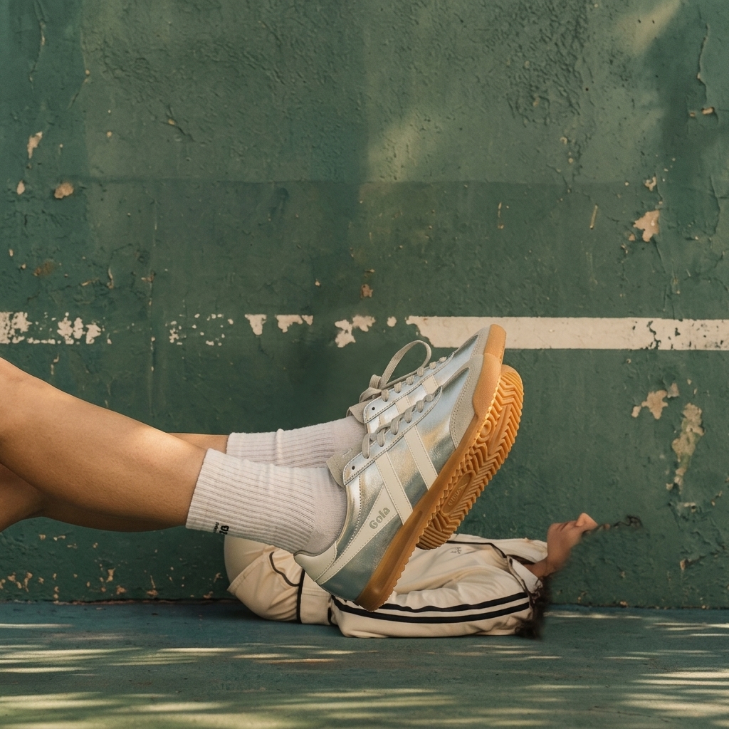 AI-generated editorial ad for Gola: silver sneakers worn cross-legged against a weathered green court wall, styled like a fashion campaign
